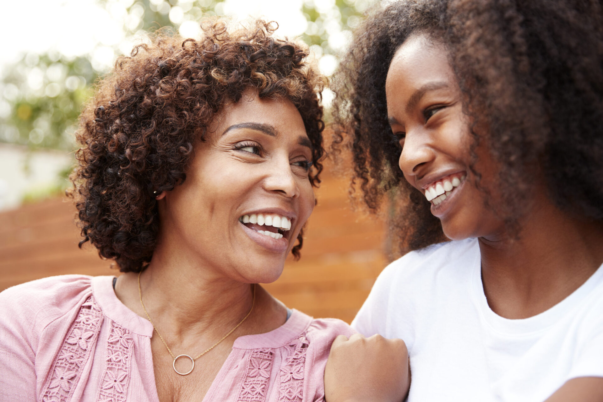 Middle aged black mom and teen daughter smiling at each other