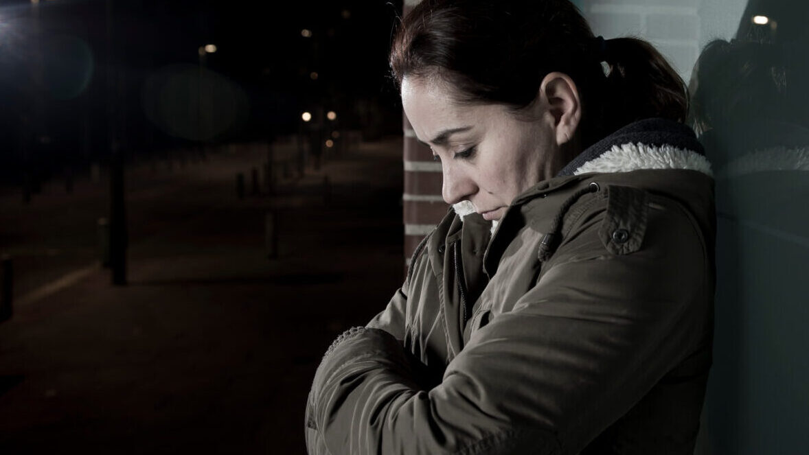 A women huddles against a wall in the cold of night 