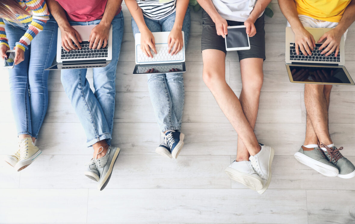 Overhead shot of a line of students on different devices -- phones, laptops, tablets.