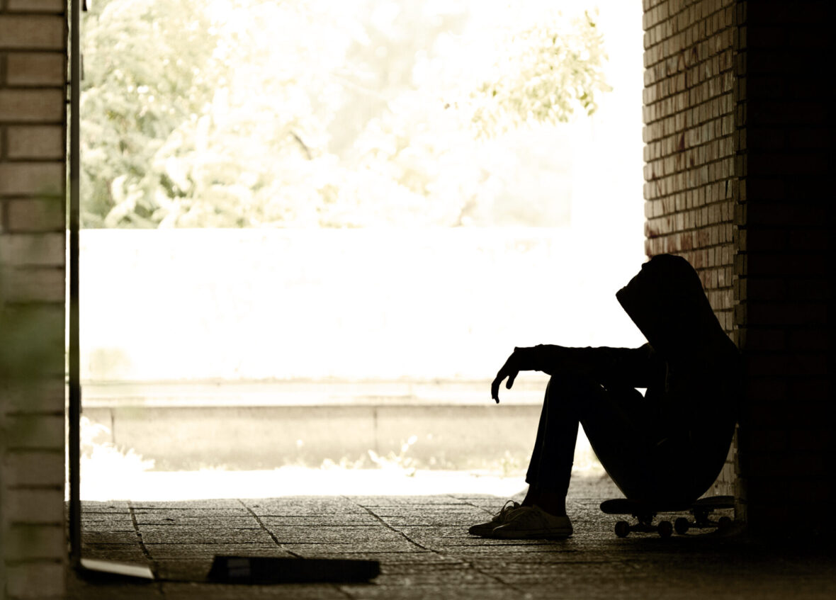 Silhouette of Lonely Teenager Sitting in the Dark Doorway