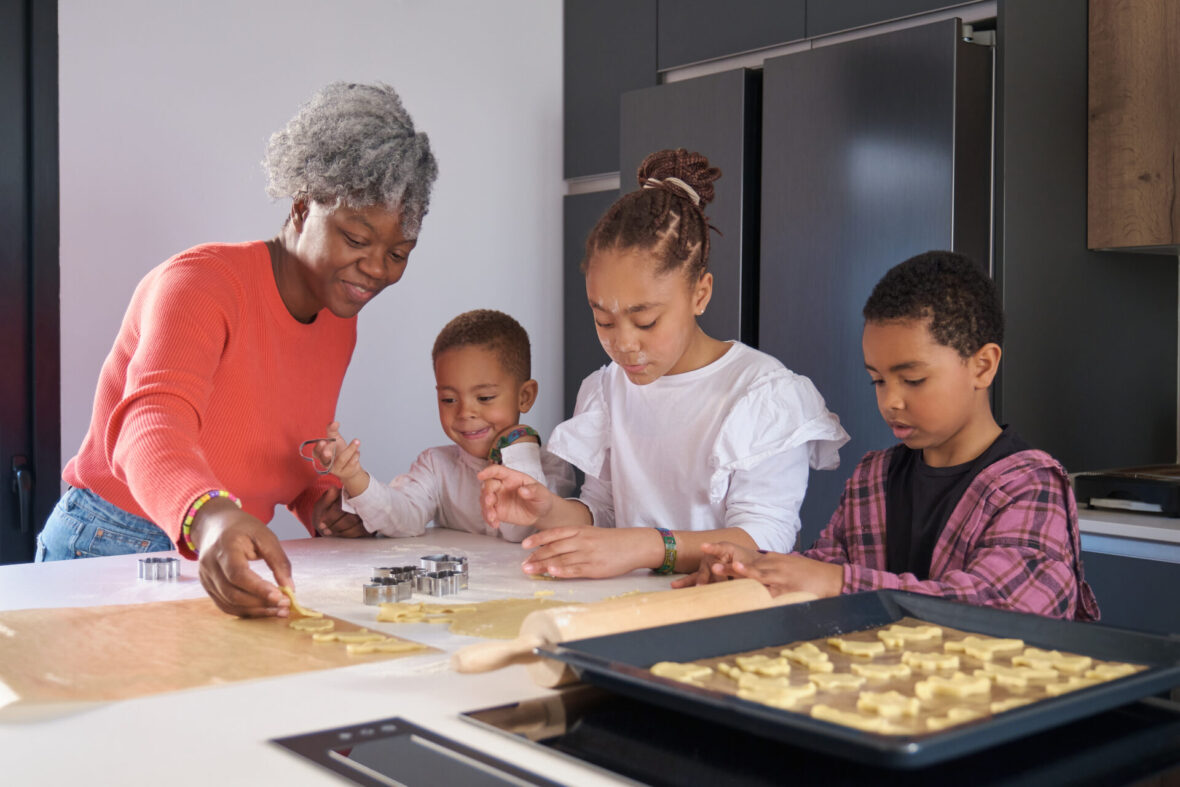 Happy african mother and children cutting cookie shapes in a cookie dough in the kitchen.